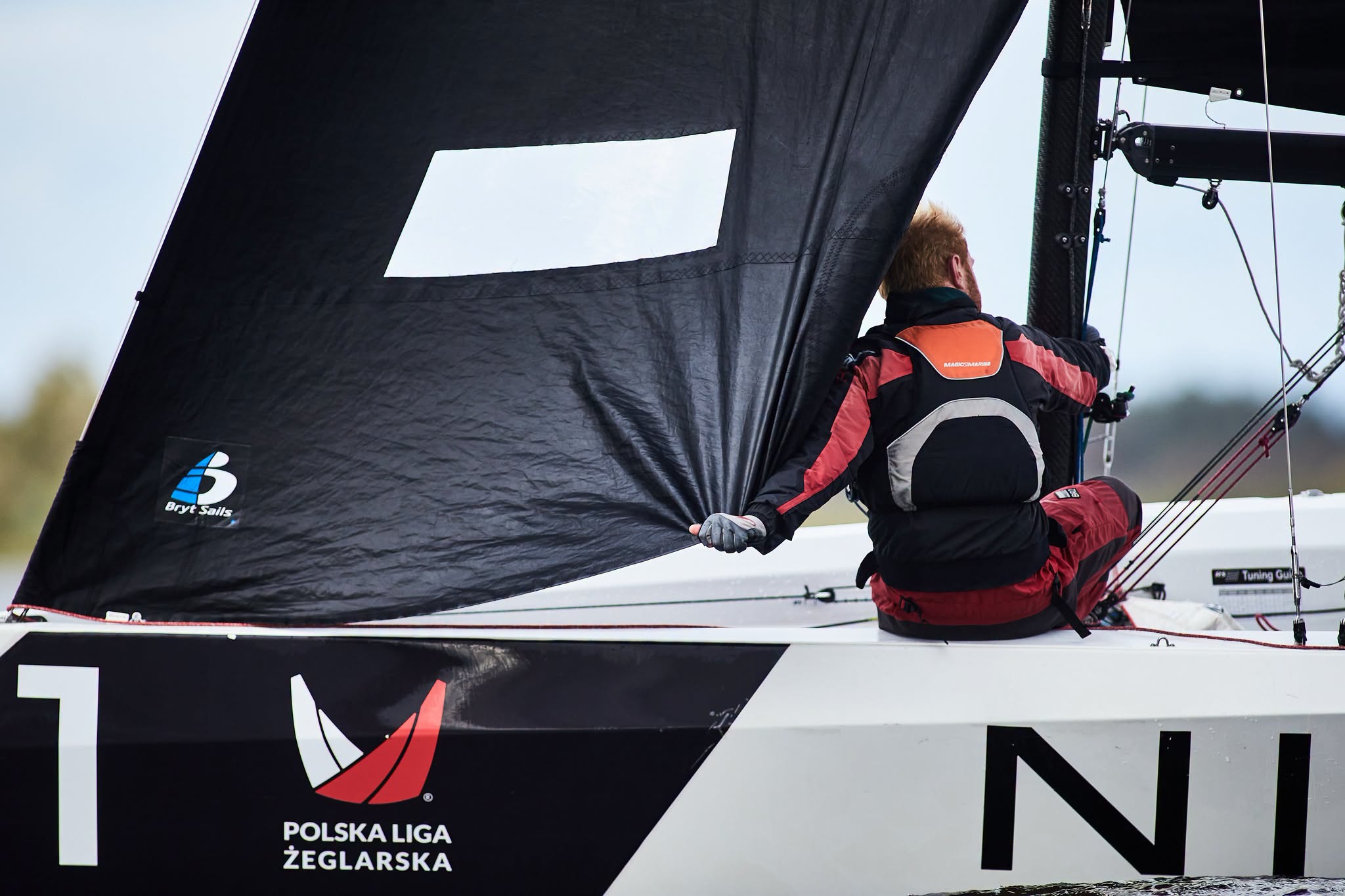 Członek załogi przy czarnym żaglu jachtu RS21 podczas manewru