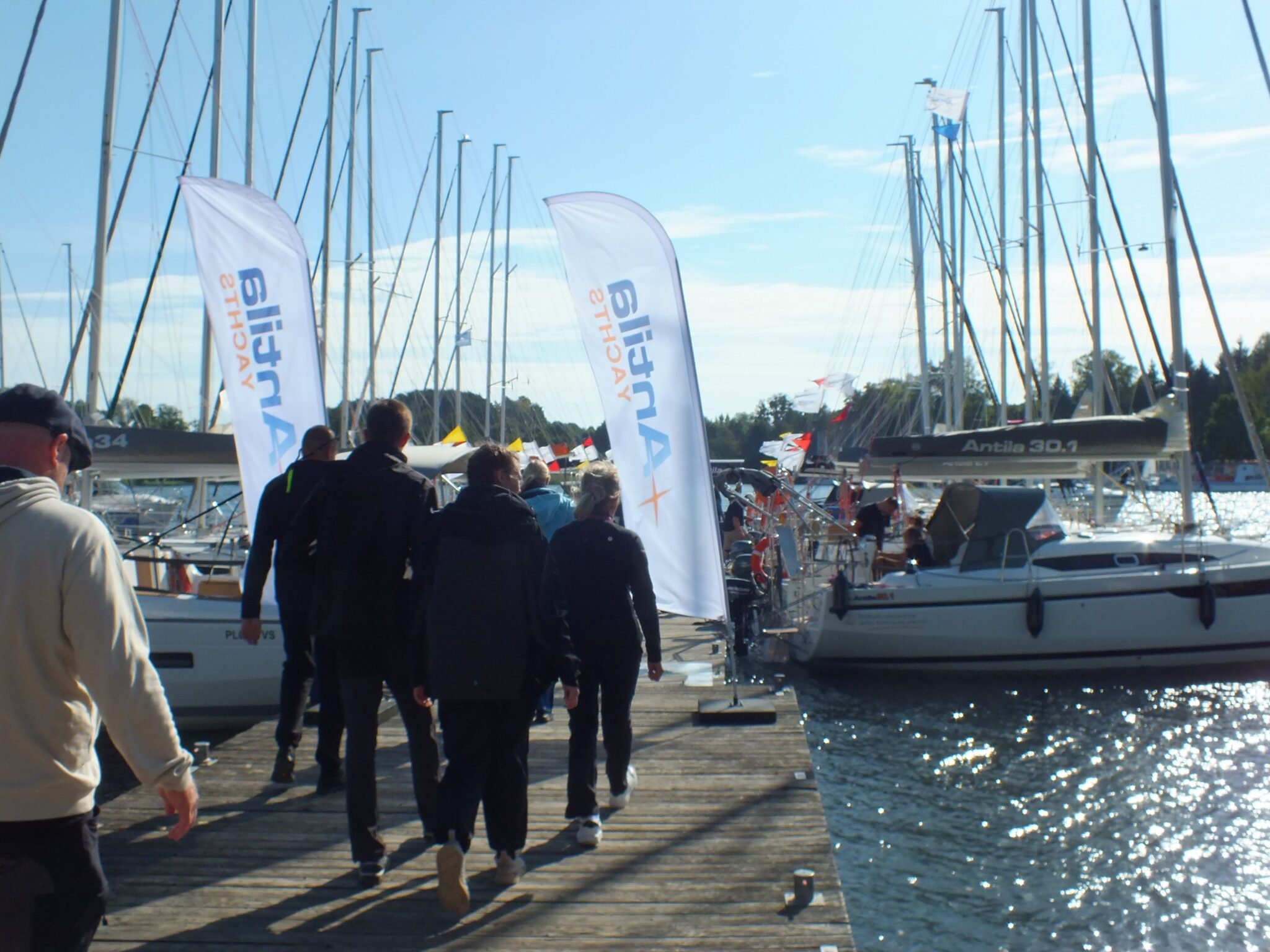 Żeglarze idą pomostem między jachtami i flagami Antila Yachts