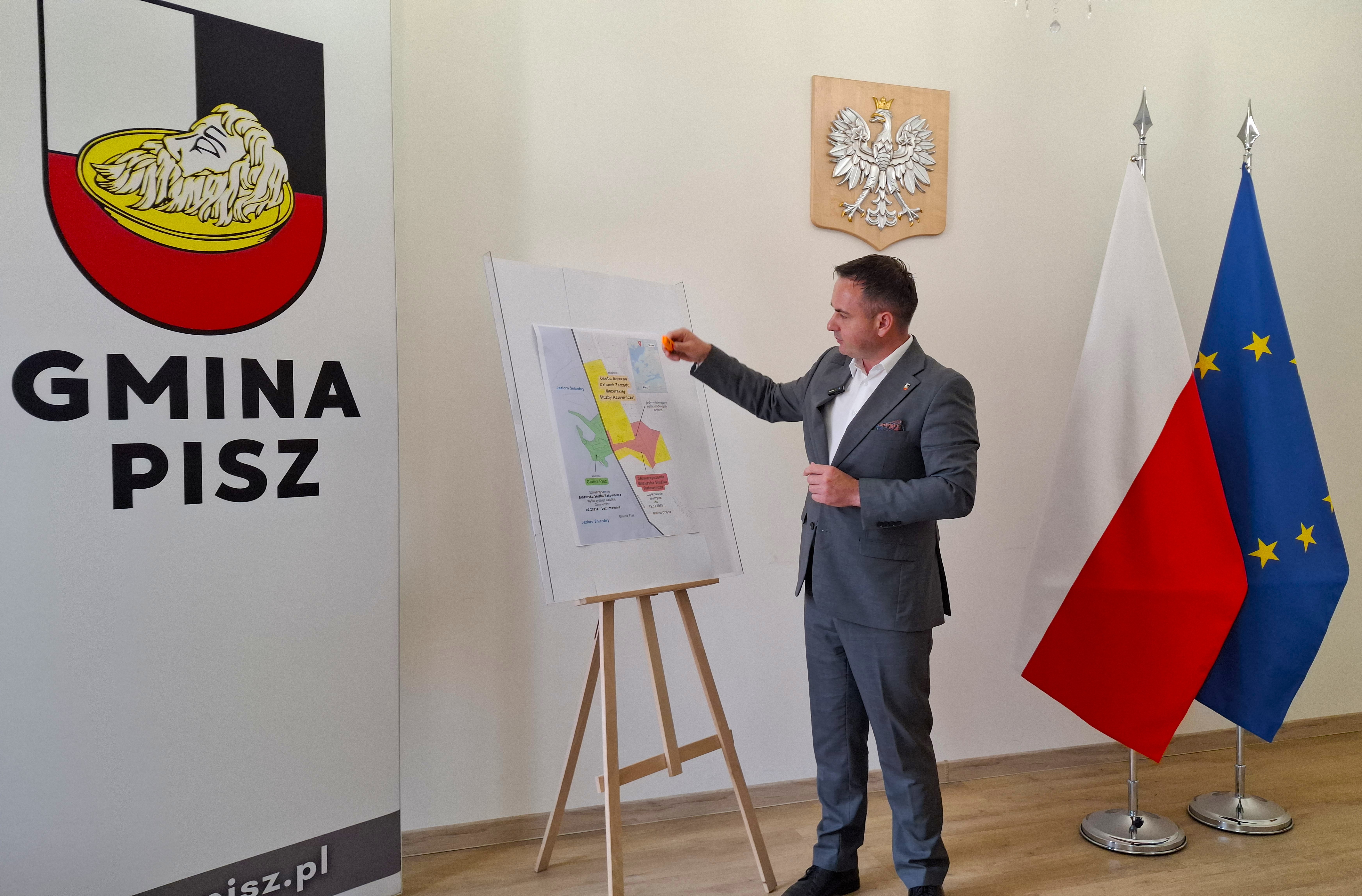 Burmistrz Pisza Dariusz Kiński omawia mapę własności działki nad Śniardwami podczas konferencji prasowej