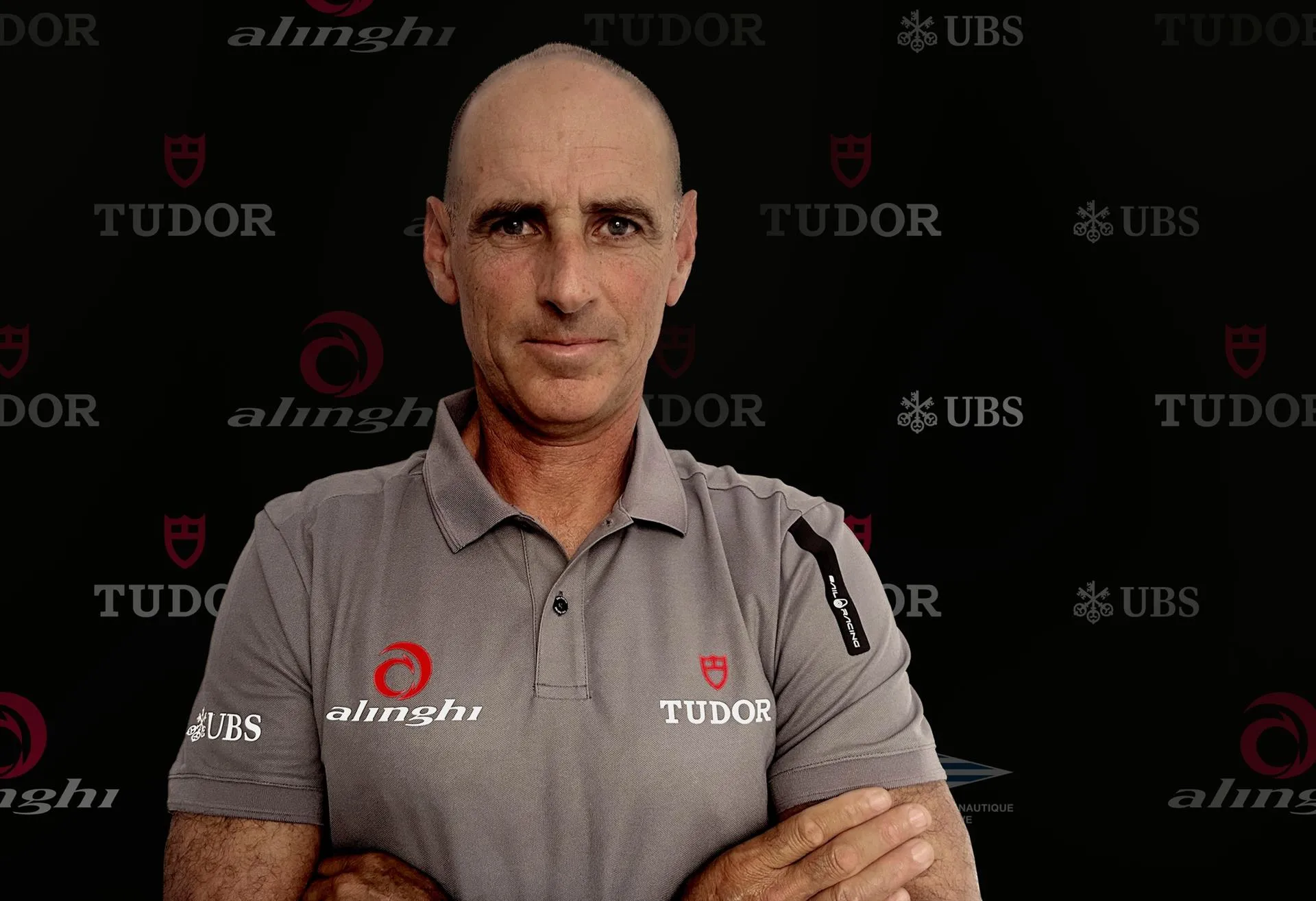 Francesco Bruni w koszulce Tudor Team Alinghi na tle ścianki z logo zespołu i sponsorów