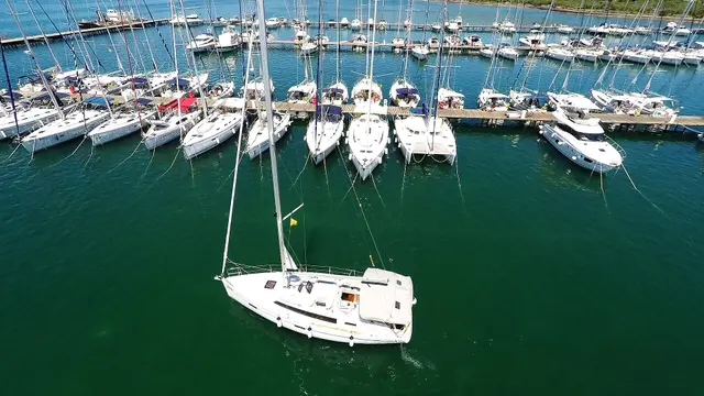 Widok z góry na marinę Punat w Chorwacji: rzędy jachtów żaglowych przy pomostach i jeden jacht wypływający z mariny