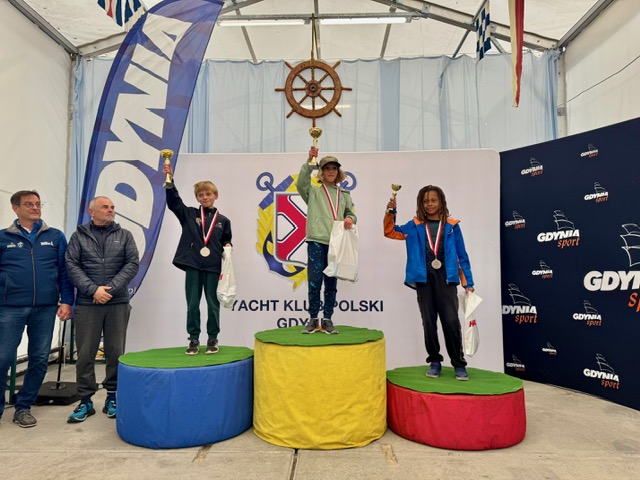 Troje młodych żeglarzy klasy Optimist z pucharami na podium w Yacht Klubie Polski Gdynia