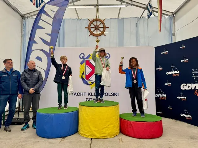 Troje młodych żeglarzy klasy Optimist z pucharami na podium w Yacht Klubie Polski Gdynia