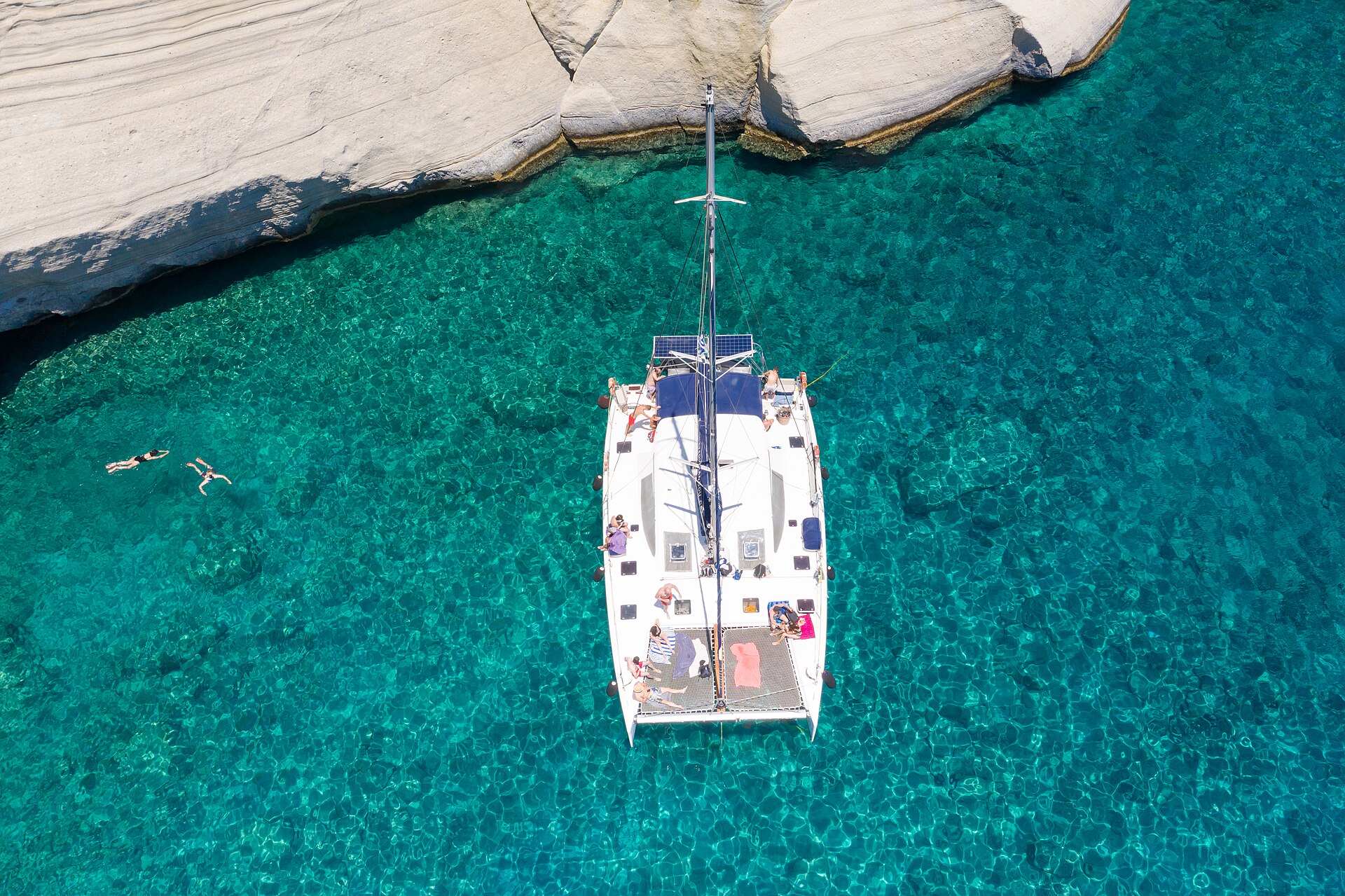 Widok z drona na katamaran żaglowy w turkusowej wodzie przy białych skałach Kleftiko na wyspie Milos w Grecji