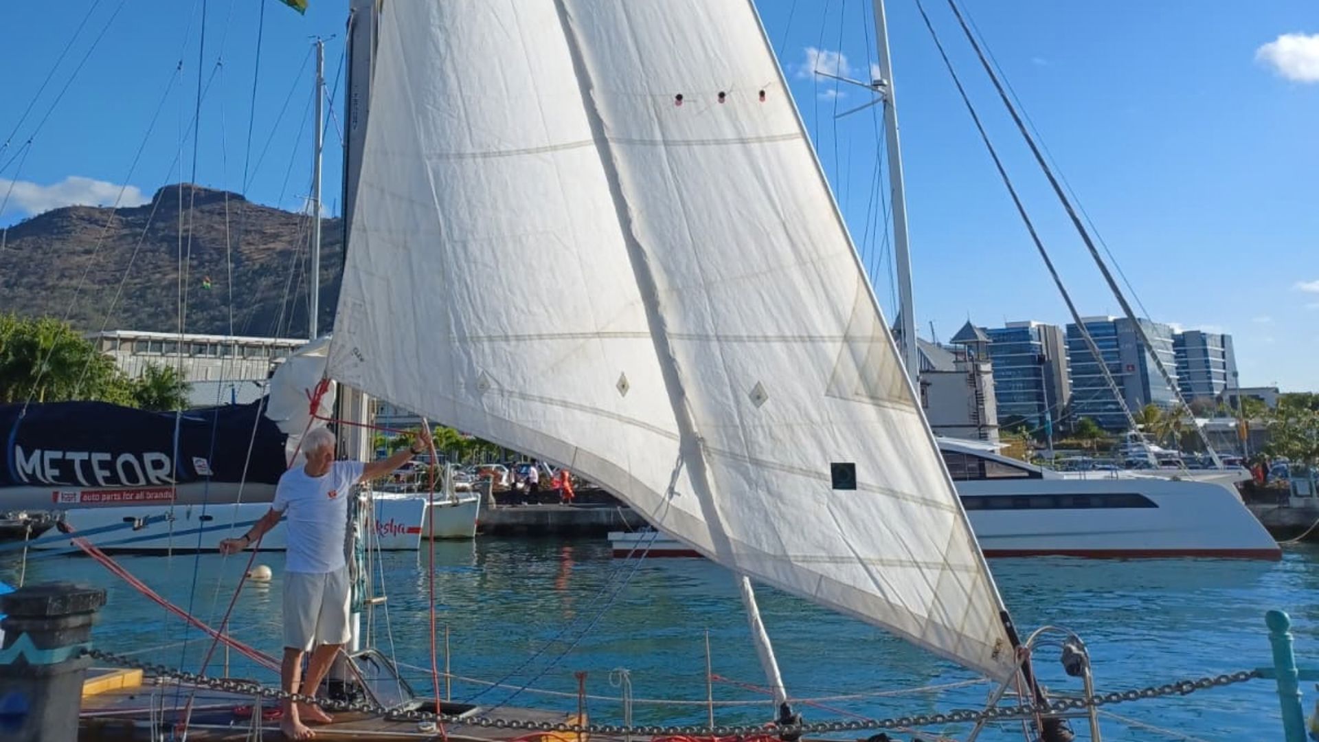 Żeglarz na dziobie jachtu Meteor przy postawionym żaglu przednim w marinie Port Louis