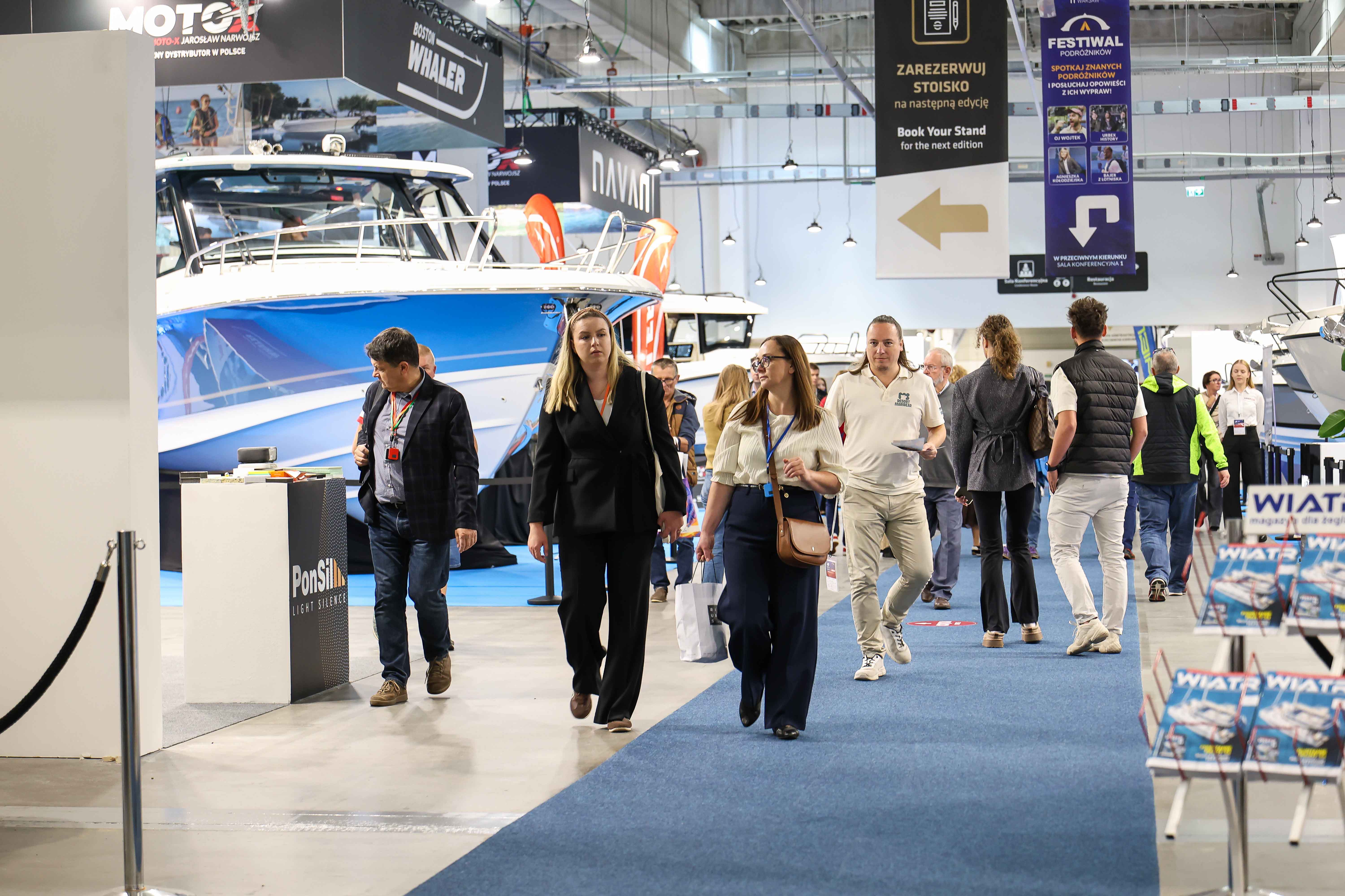 Zwiedzający mijają dużą niebieską motorówkę w hali Poland Boat Show