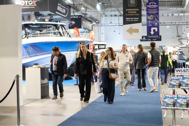 Zwiedzający mijają dużą niebieską motorówkę w hali Poland Boat Show