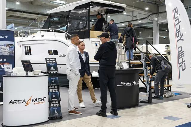 Zwiedzający rozmawiają przy białym jachcie motorowym Stillo Yachts w hali targowej
