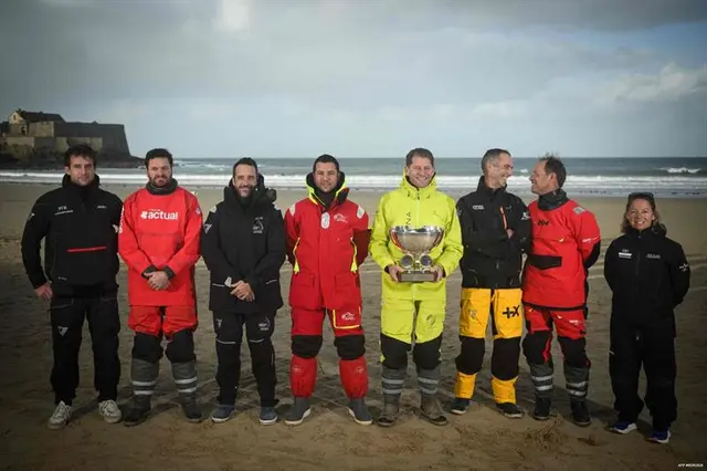 Ośmioro skipperów klasy Ultim w sztormiakach, z pucharem, na plaży w Saint-Malo