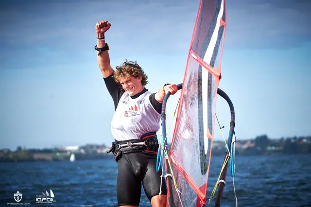 Windsurfer w koszulce MŚ U23 iQFOiL unosi pięść na wodach Zatoki Puckiej