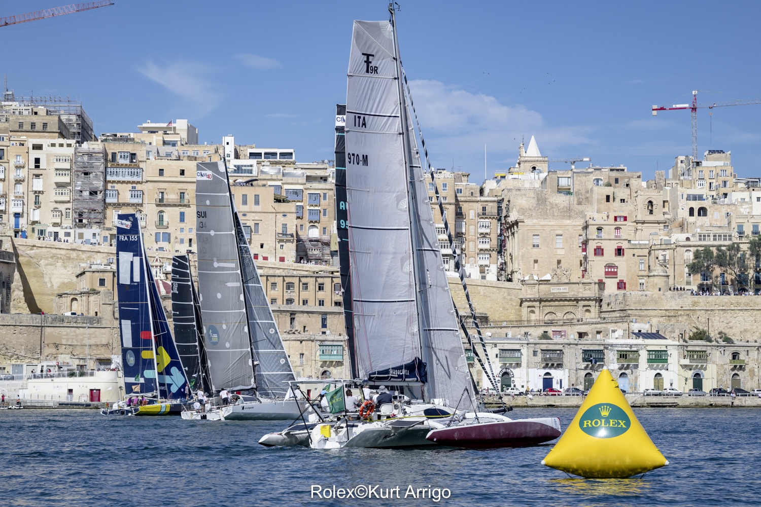 Trimaran Farrier F9AX Turbolenta na starcie przy boi Rolex, w tle zabudowa Valletty