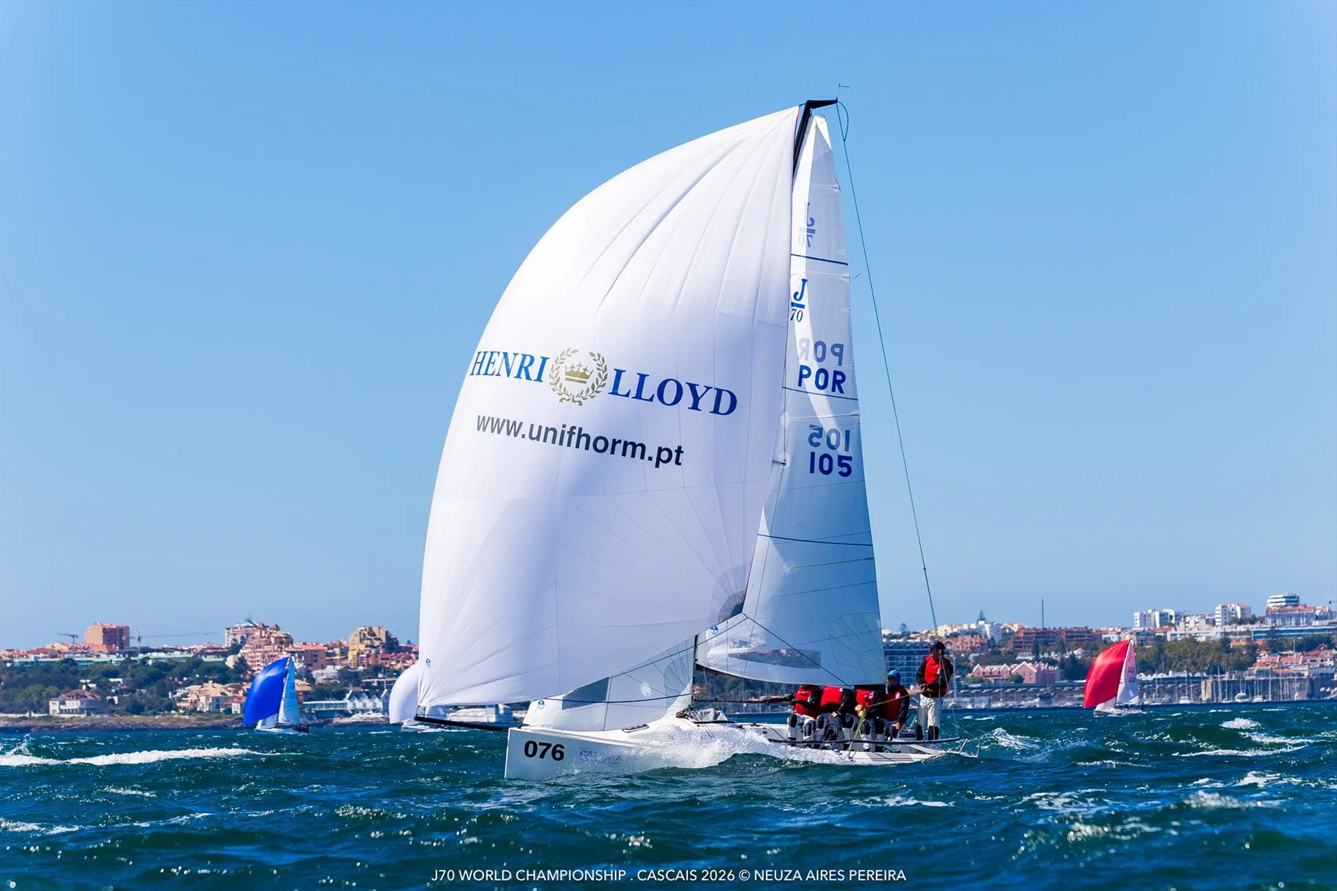 Portugalski jacht J/70 z rozwiniętym spinakerem na kursie z wiatrem przed panoramą Cascais