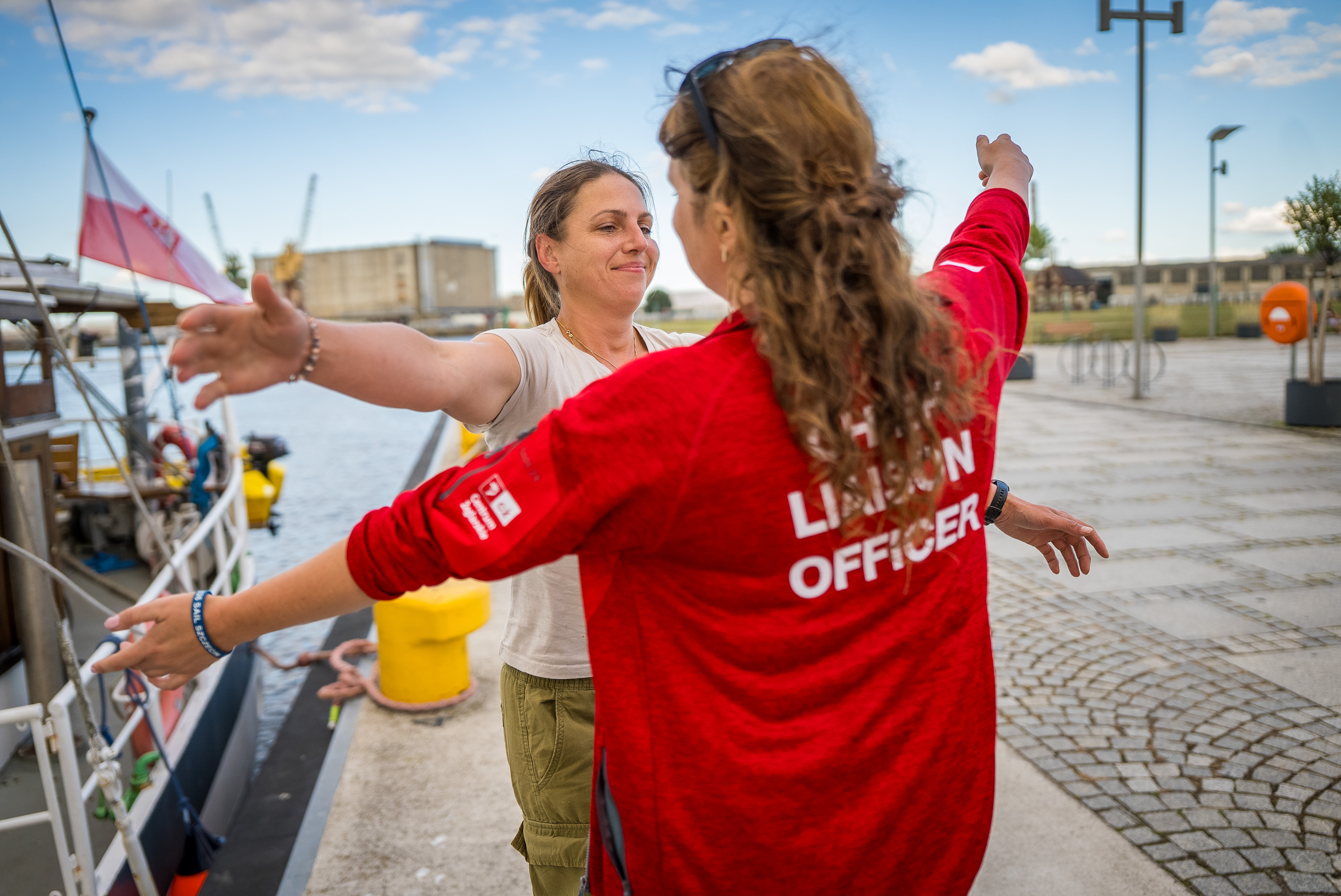 Oficer łącznikowa w czerwonej koszulce wita członkinię załogi przy jednostce