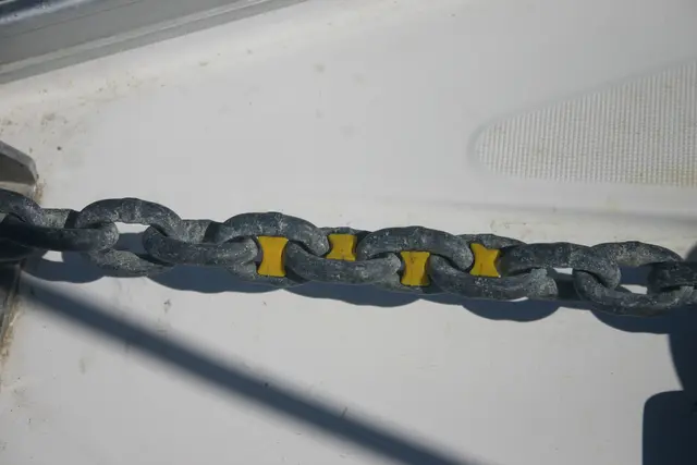 Łańcuch kotwiczny na pokładzie jachtu z plastikowymi znacznikami wpiętymi w ogniwa, które pokazują długość wydanego łańcucha